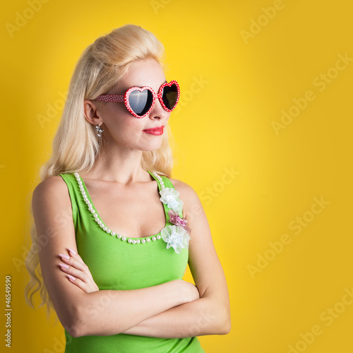 Blonde girl with heart glasses against yellow background.