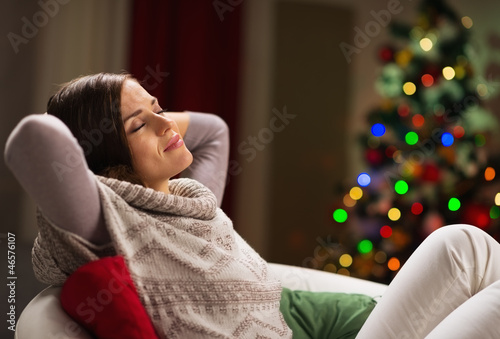 Young woman relaxing on chair in front of Christmas tree