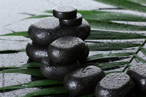Spa stones with drops on green palm leaf on grey background