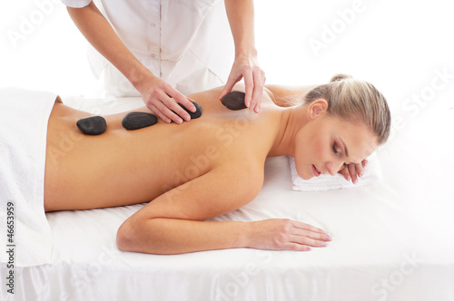 Back of a young woman laying on a lava stone massage procedure