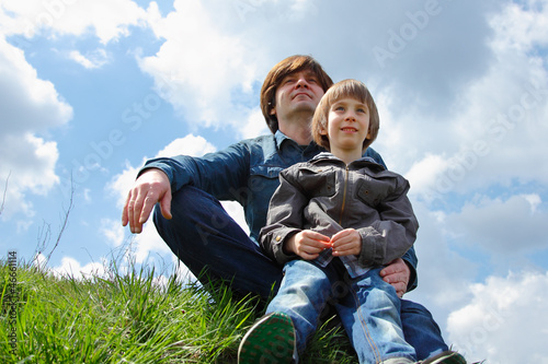 happy father with little son sitting on green grass and looking