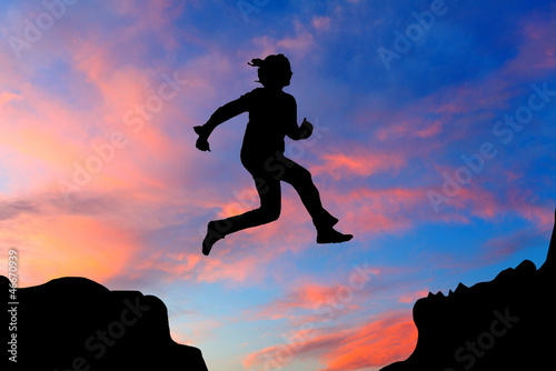 Silhouette of hiking woman jumping over the mountains at sunset