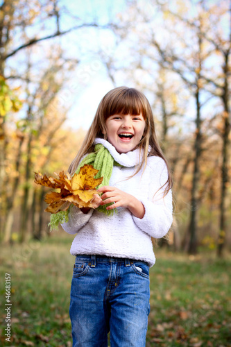 Happy little girl with maple leaves in autumn forest outdoors