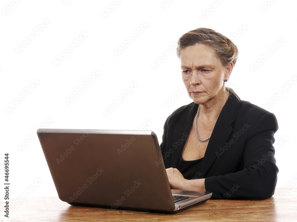 Mature woman sitting by table working on notebook computer Mature woman sitting by table working on notebook computer