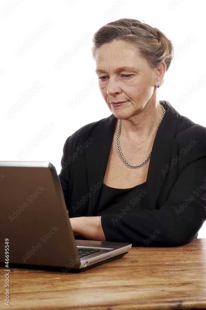Mature woman sitting by table working on notebook computer Mature woman sitting by table working on notebook computer