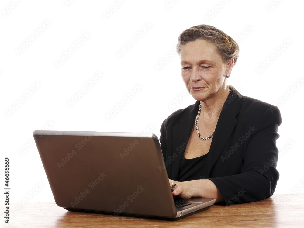 Mature woman sitting by table working on notebook computer Mature woman sitting by table working on notebook computer