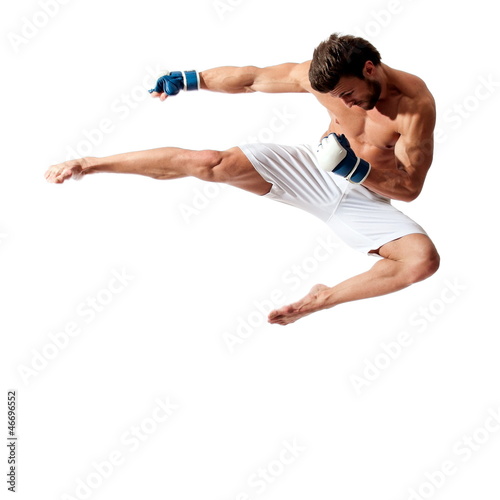 Young fit man jumping, high kick and fist punch, muay thai equipment.