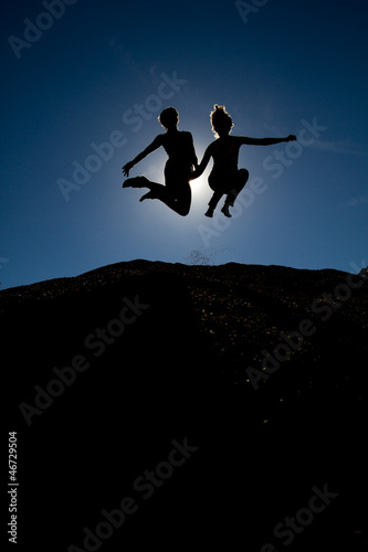 silhouette of couple jumping on top of hill