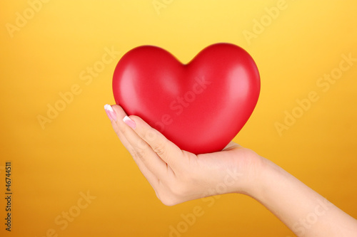 Red heart in woman s hand  on orange background close-up