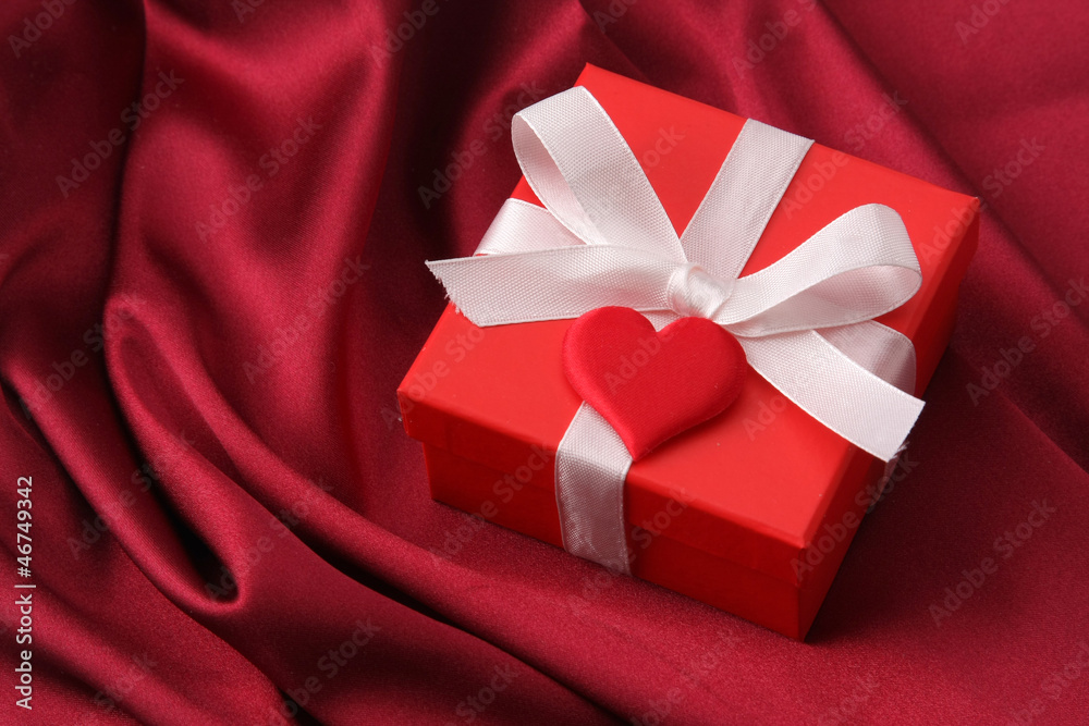 A gift with a red ribbon and heart on red silk A gift with a red ribbon and heart on red silk