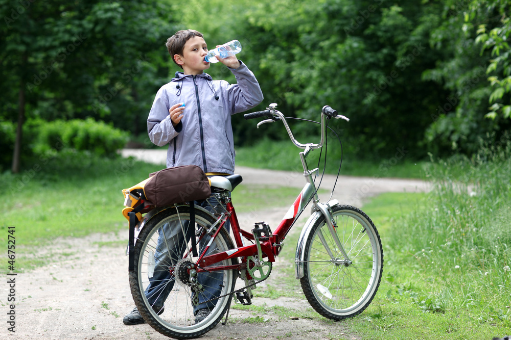 Young boy with bicycle with drinking clear water Young boy with bicycle with drinking clear water