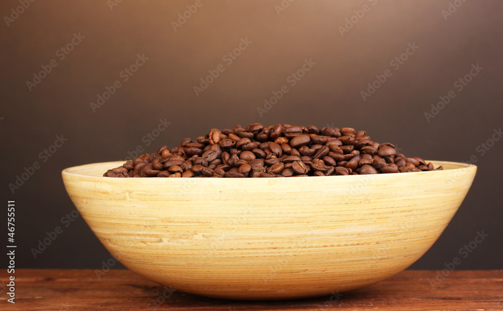 Coffee beans in bamboo bowl on table on brown background Coffee beans in bamboo bowl on table on brown background