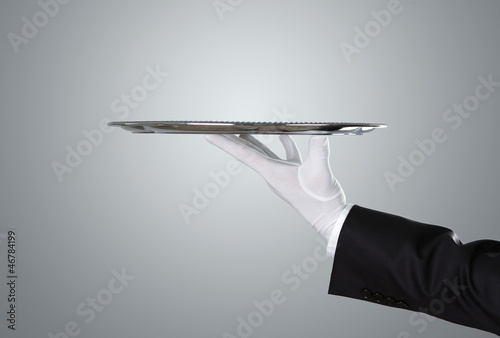 Waiter holding empty silver tray over gray background with copy
