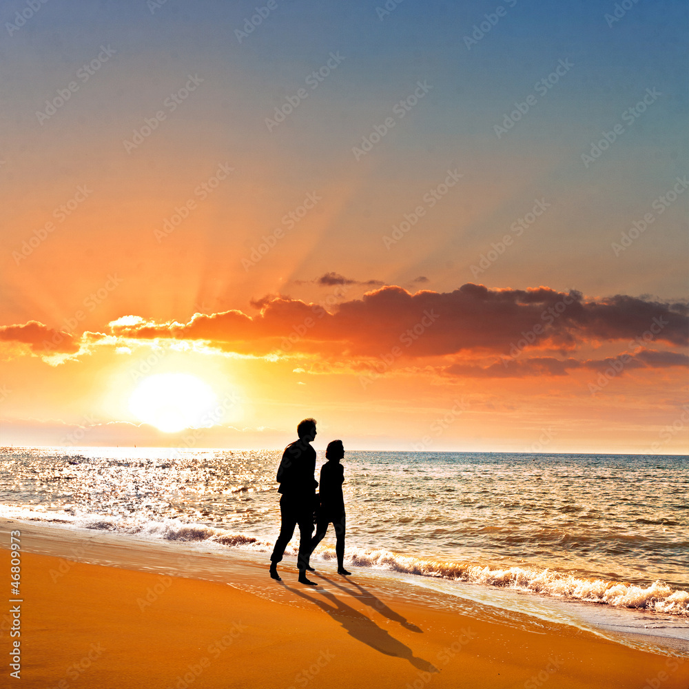 Young couple walking on the beach at sunset.