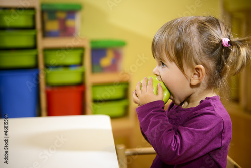 female child eating green apple in kindergarten