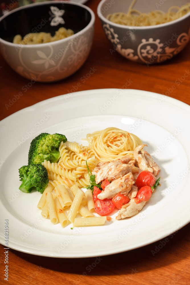 Dinner of vegetables pasta tomato and chicken on a white plate.