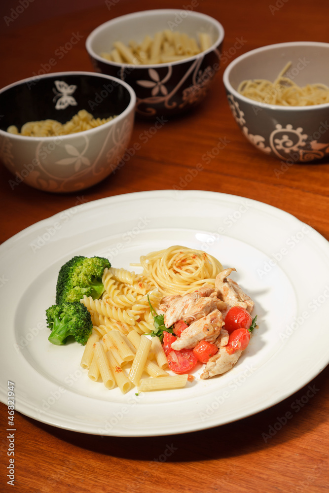 Dinner of vegetables pasta tomato and chicken on a white plate.