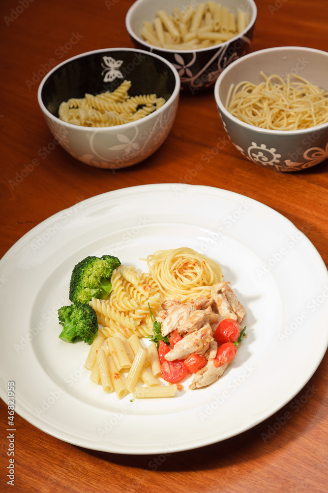 Dinner of vegetables pasta tomato and chicken on a white plate.