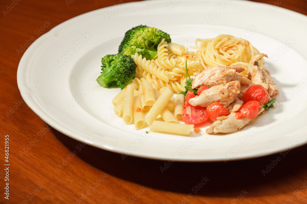 Dinner of vegetables pasta tomato and chicken on a white plate.