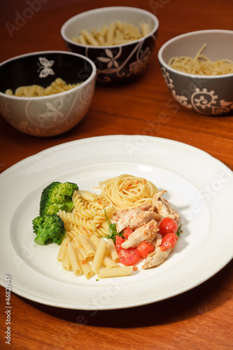 Dinner of vegetables pasta tomato and chicken on a white plate.