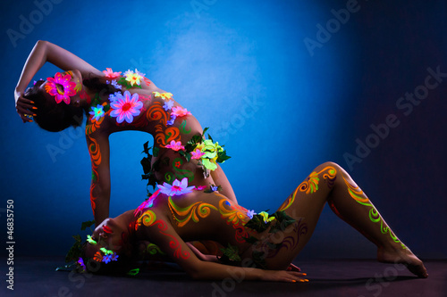 Nude women with glow uv body art and flowers