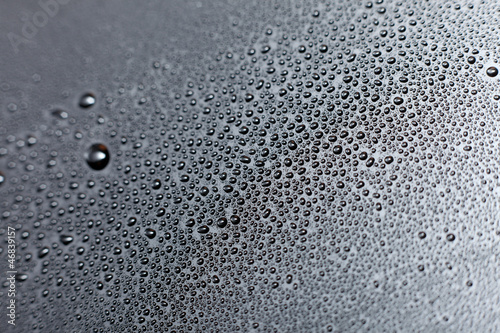 Close-up of water drops on black reflective surface.