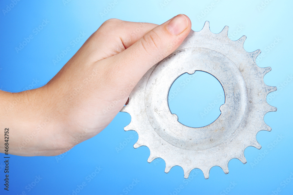 Man holding metallic cogwheel in his hand on blue background Man holding metallic cogwheel in his hand on blue background