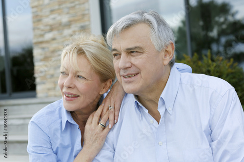 Senior couple sitting in front of house and looking away