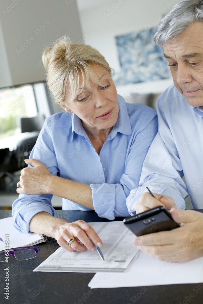 Senior couple calculting bills amount using smartphone Senior couple calculting bills amount using smartphone