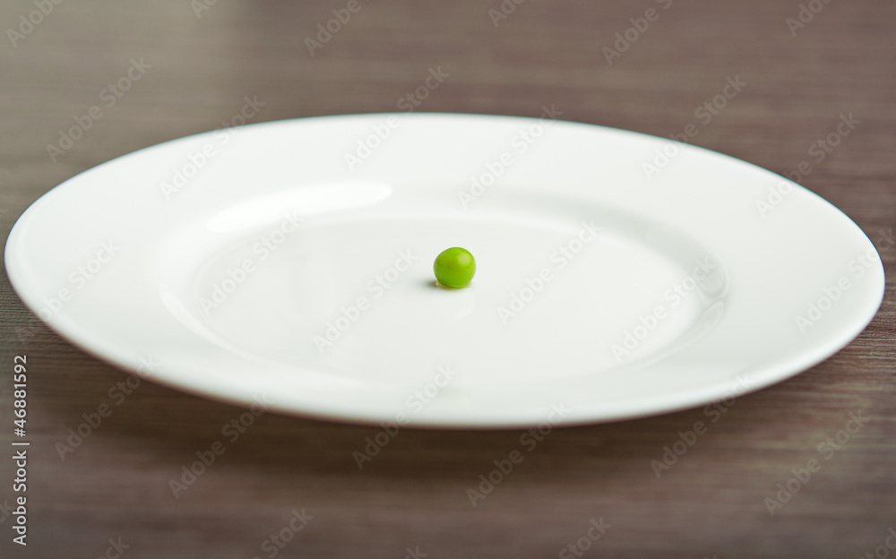 diet concept. one pea on an empty white plate diet concept. one pea on an empty white plate