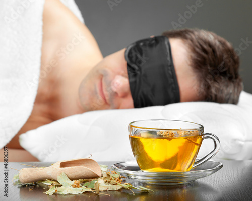 Man with Sleeping mask sleep on a bed, cup of herbal tea in the
