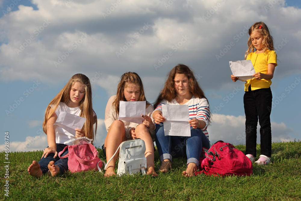 Three girls sit on grass and read something and little girl Three girls sit on grass and read something and little girl