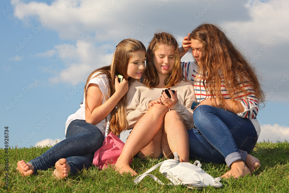 Three girls sit on grass with mobile phones