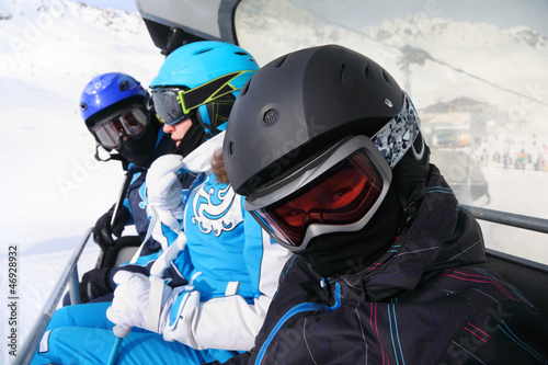 Three skiers in helmets and goggles ride on funicular