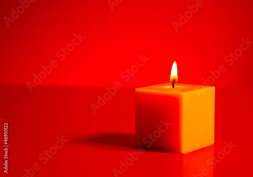 Burning yellow candle over red background