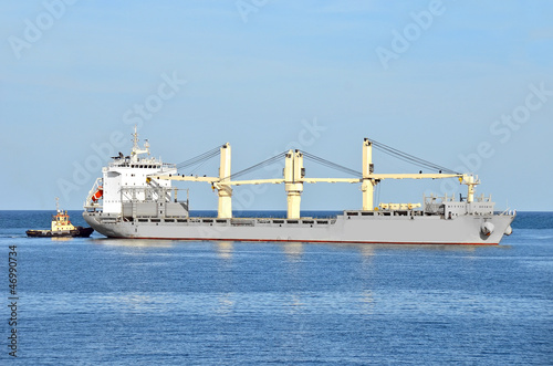 Tugboat assisting bulk cargo ship to harbor quayside