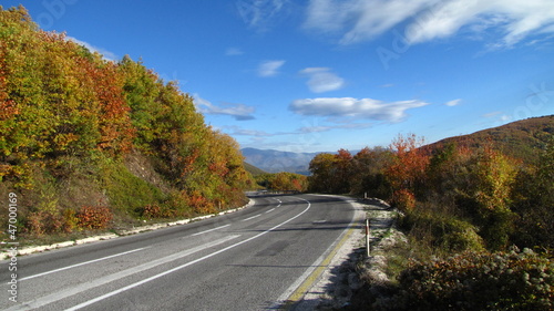 Road to an autumn mountain and white clouds on blue sky