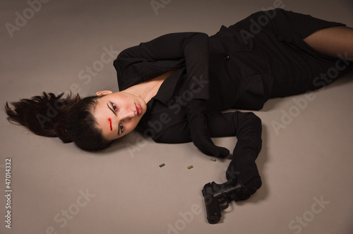 Woman in a black suit with gun lying on the floor © Demian