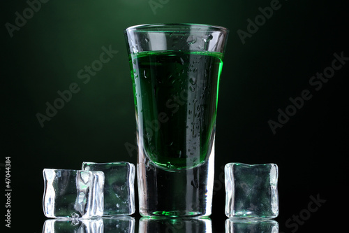 glass of absinthe and ice on green background.