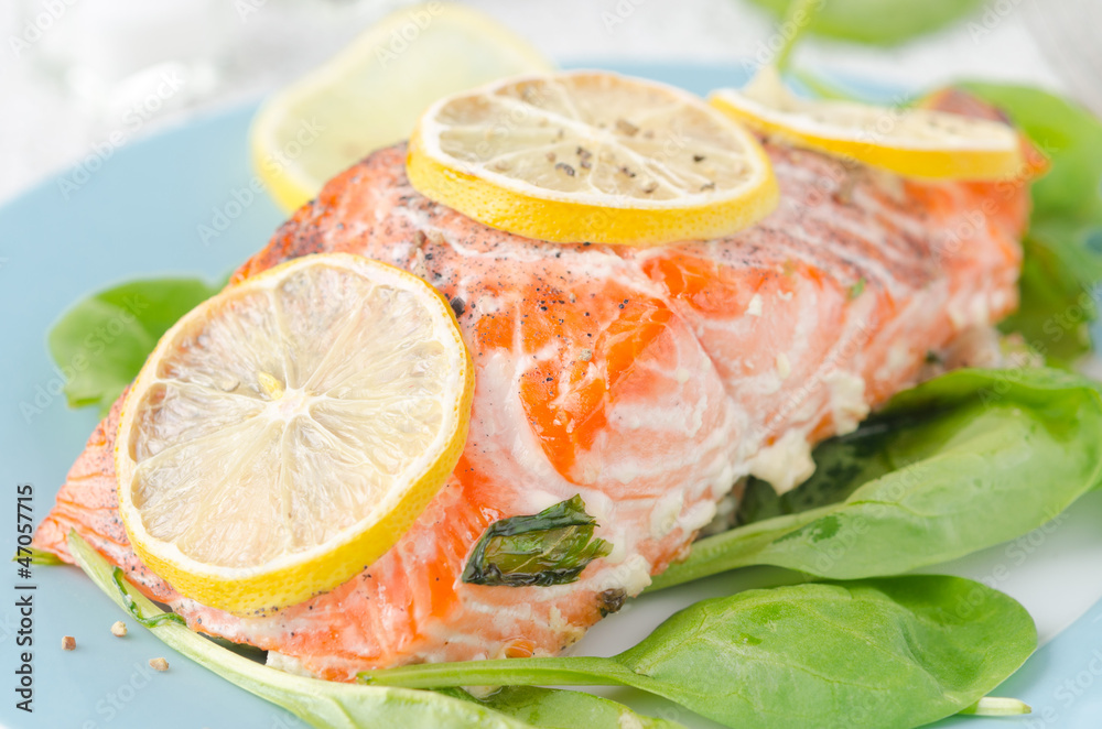 Baked salmon fillet with lemon and spinach on a plate close up