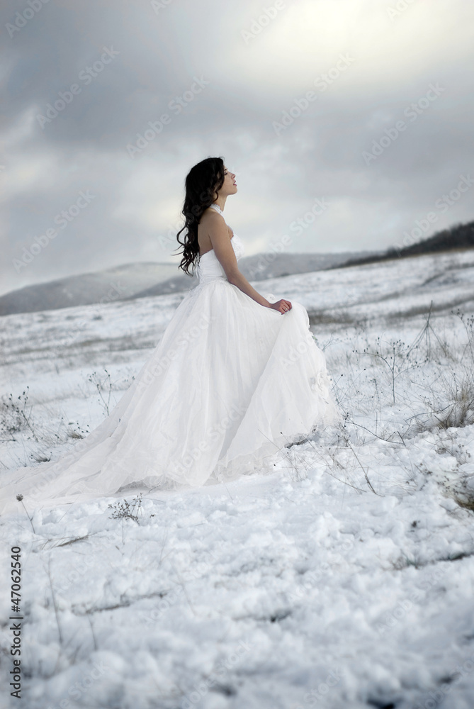 pretty young woman posing in wedding dress  on winter snow