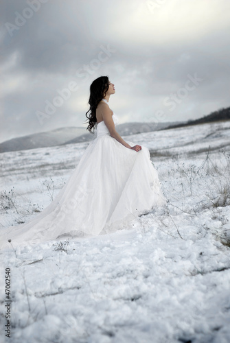 pretty young woman posing in wedding dress on winter snow