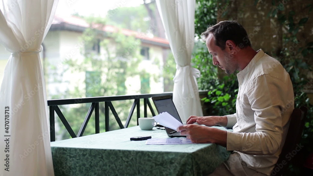 Happy man with laptop computer and documents on his balcony Happy man with laptop computer and documents on his balcony