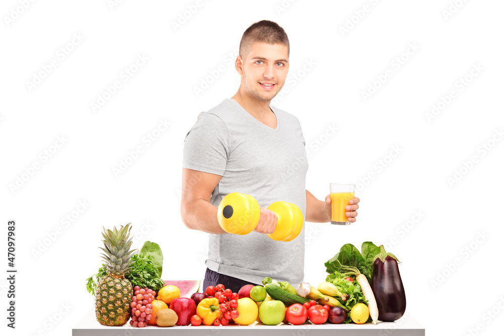 Guy holding a dumbell and glass of juice behind a pile of fruits Guy holding a dumbell and glass of juice behind a pile of fruits