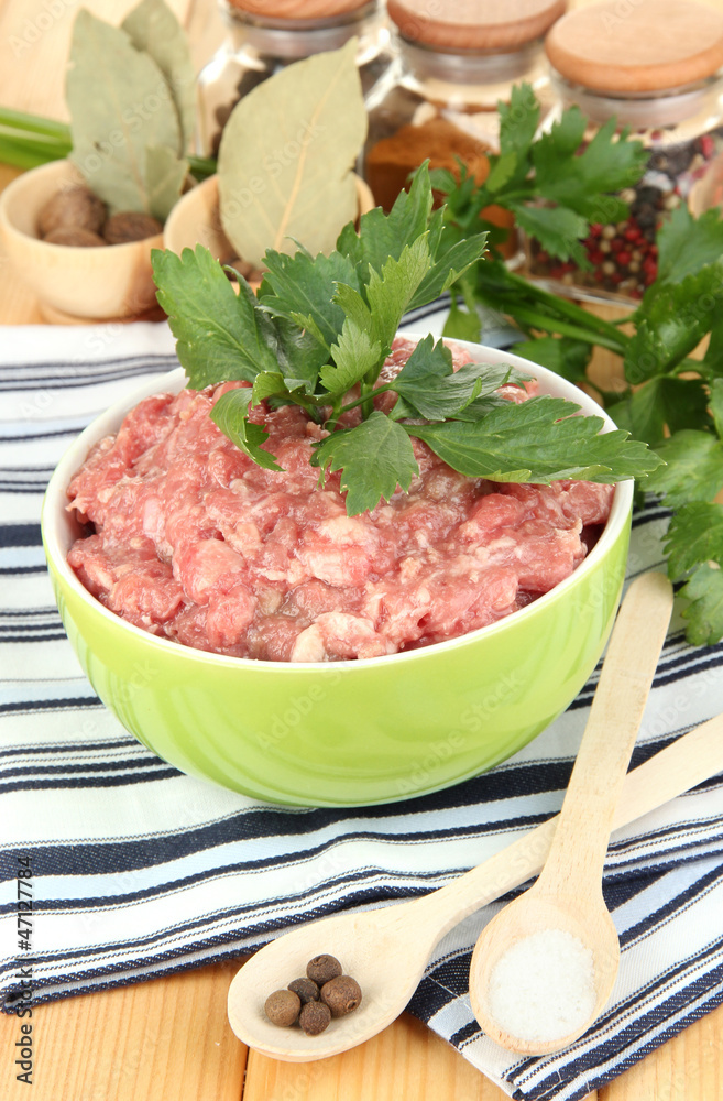 Bowl of raw ground meat with spices on wooden table