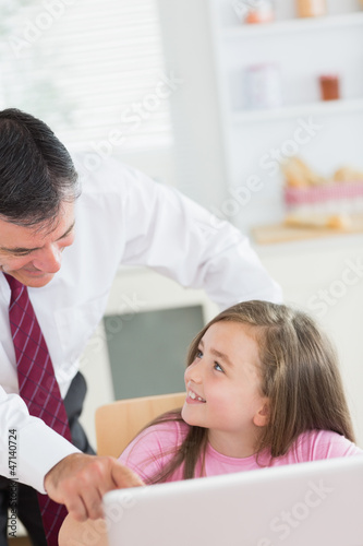 Father pointing at laptop with daughter smiling up at him