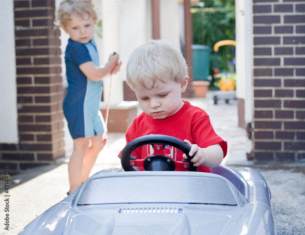 Two little brothers toddlers playing with big toy car