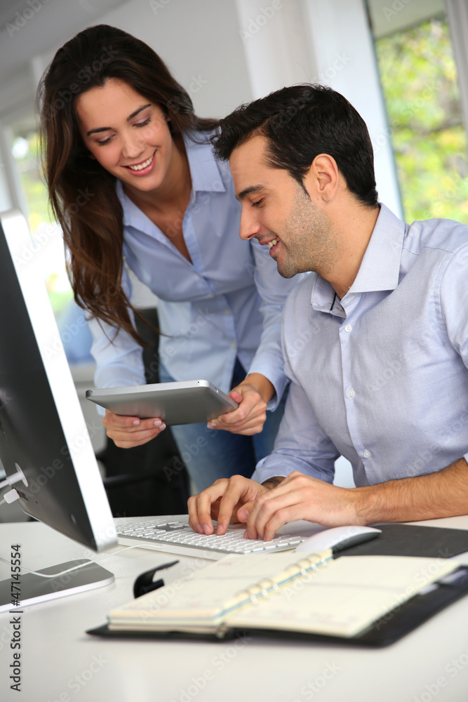 Office workers in front of desktop computer with tablet Office workers in front of desktop computer with tablet