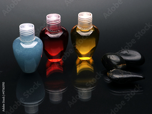 Colorful shampoo set and stones on reflected black surface