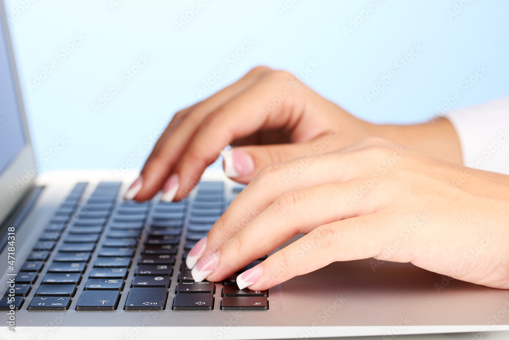 Hands typing on laptop keyboard close up on blue background Hands typing on laptop keyboard close up on blue background